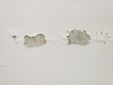 A damaged white wall showing severe peeling paint and bubbling from moisture or water leakage revealing raw plaster.
