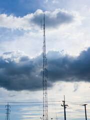Obraz premium A tall telecommunication mast stands against a dramatic cloudy sky with sunlight peeking through dark clouds.