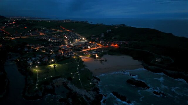 Drone view of a coastal village and sandy bay illuminated at blue hour in Santander Spain