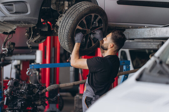 Auto mechanic changing a tire on a raised car in a garage, performing wheel service and vehicle maintenance