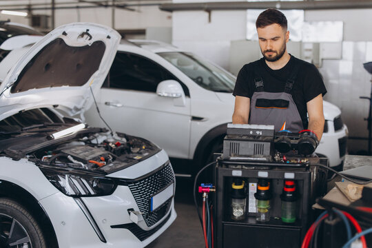 Car mechanic diagnosing vehicle with open hood in auto repair shop, performing maintenance service on modern car