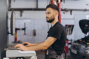 Obraz premium Auto technician performing digital car diagnostics on a monitor, checking vehicle systems in a modern professional workshop
