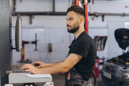 Auto technician performing digital car diagnostics on a monitor, checking vehicle systems in a modern professional workshop