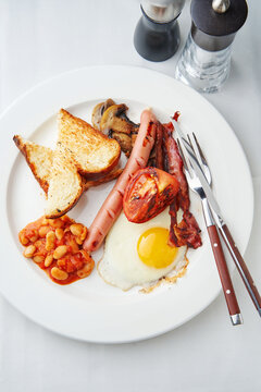 Full breakfast plate with eggs, sausages, beans, toast, and grilled tomato, hearty meal for dining or food delivery service