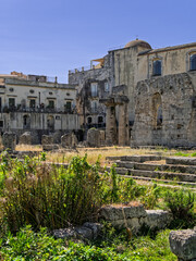 Obraz premium Vertical image of the Temple of Apollo with the San Paolo Apostolo church background in Ortigia, Syracuse, Italy. Historic archaeological site and old town buildings in Sicily.