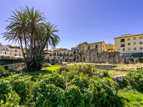The historic Greek Temple of Apollo surrounded by green gardens and palms in Pancali Square, Ortigia. Travel photography of famous ancient monument ruins in Syracuse, Sicily.