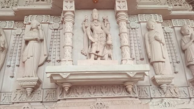 Tilt up shot of Lord Indra idol and traditional stone carvings on the facade of a pink sandstone Hindu temple