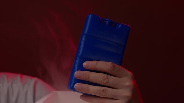 Close-up of hand removing very cold blue plastic ice pack from portable freezer, with visible vapor rising from extremely low temperature, suggesting cryopreservation, organ transport, slow motion