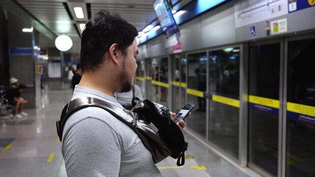 an asian man using mobile smartphone while waiting for upcoming subway train at train station, man use smartphone social media in public subway underground train