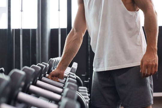 Fitness man in training showing exercises with dumbbells in gym.