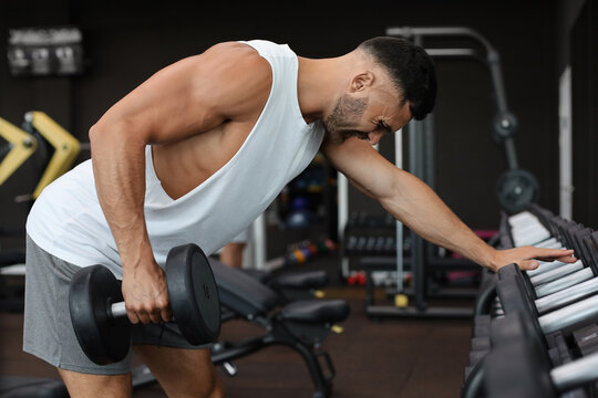 Fit and muscular man trains with dumbbells.