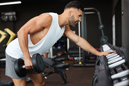 Fit and muscular man trains with dumbbells.