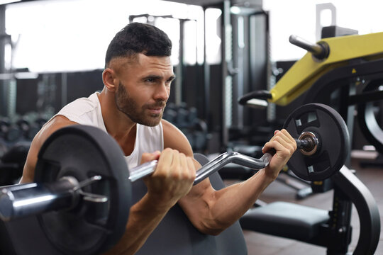 Fit and muscular man lifting heavy barbell weight using bench at the gym.