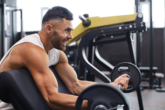 Fit and muscular man lifting heavy barbell weight using bench at the gym.