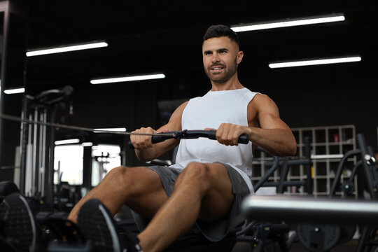 Fit and muscular man using rowing machine at gym.