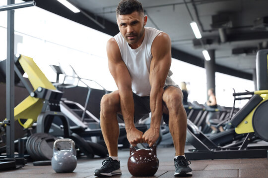 Fit and muscular man focused on lifting a dumbbell during an exercise class in a gym.