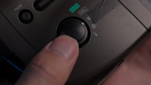 Close-up of operator finger turning mode selector dial on old analog camcorder, choosing between various settings like auto, manual, sports, portrait, low light for retro filming experience, slowmo