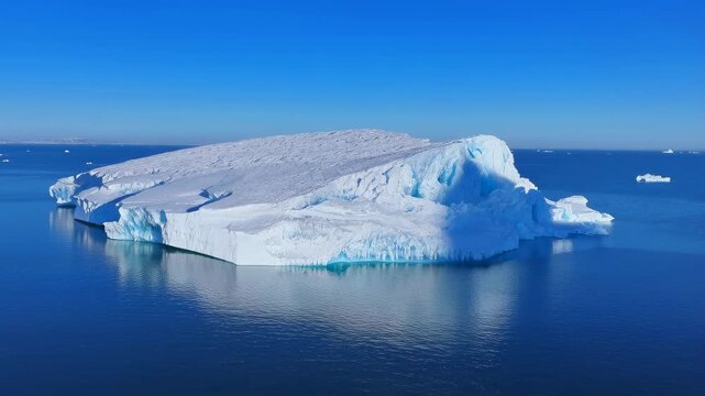 Aerial view of a massive iceberg floating in calm blue waters. Represents the beauty and fragility of polar environments and climate change awareness