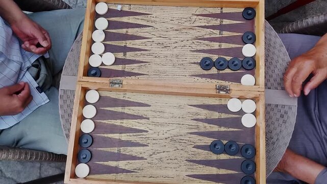 4k video footage of two men Playing backgammon at the coffee shop with hearing oriental songs, outdoor activity. using Dices to get number of movements of checkers and following the game rules, select