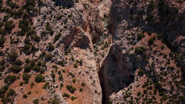 Drone footage tilting down into El Chorro's split rock face, exposing the concealed boardwalk path, jade river glimpse, and scattered pine dotting sun-bleached canyon walls.
