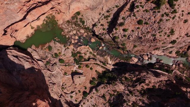 Drone footage twisting straight down into El Chorro's canyon floor, exposing emerald rock pools, white water, a narrow cliff path, and sun-scorched boulders in vivid detail.