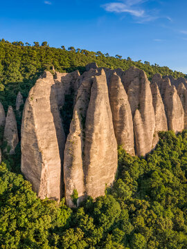 Aerial view of the Penitents des Mees rock formation, with eroded sandstone spires rising above forested slopes in Alpes-de-Haute-Provence. French Alps, France