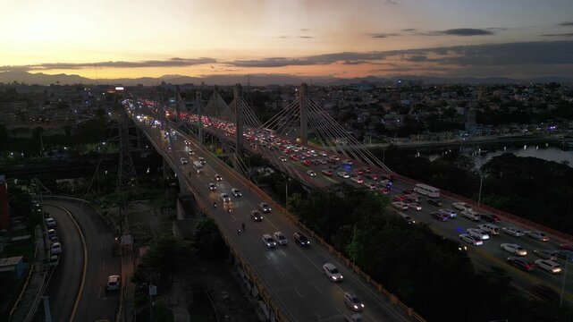 Heavy traffic jam on Puente Juan Pablo Duarte and Juan Bosch bridge over river at sunset in Santo Domingo, Dominican Republic. Aerial drone panoramic view