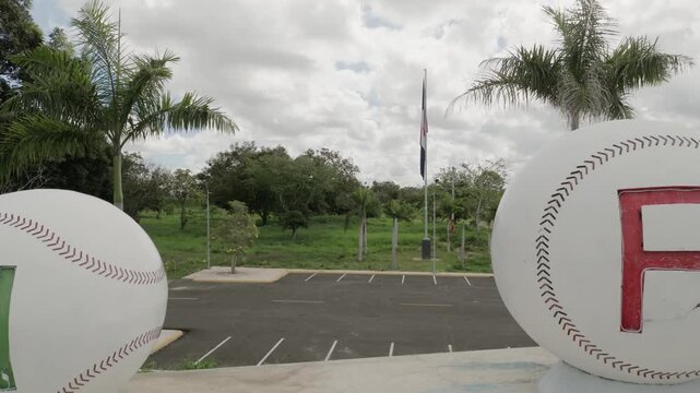 Drone flying backward between white baseballs of monument at entrance of San Pedro de Macoris, Dominican Republic