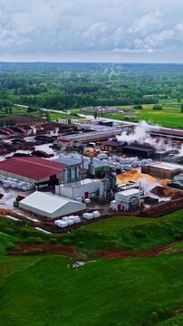Vertical aerial view of the Stora Enso wood processing sawmill in Launkalne, Latvia, showing industrial buildings, lumber yard storage, and steam emissions surrounded by green forests