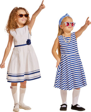 Two girls pointing upward in sunglasses on transparent background. Concept of kids summer fashion, nautical style, vacation advertising, friendship, playful direction.