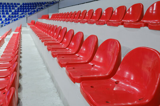 Rows of empty red plastic seats in a stadium tribune.
