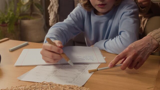 Handheld shot of Caucasian child writing in notebook while senior woman guides him with pen during home study. Clip is perfect for promoting elementary tutoring or homeschooling programs