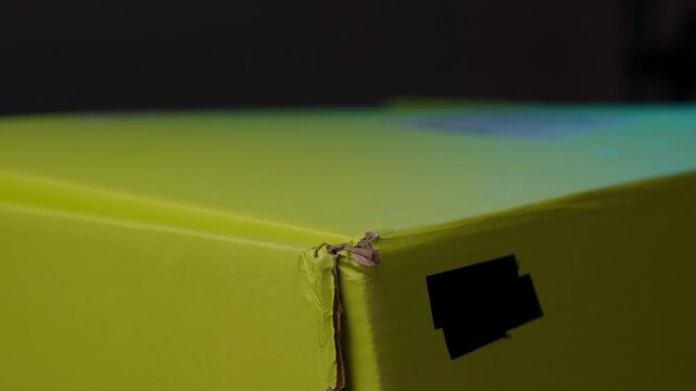 Close-up of hand pulling black adhesive tape off vibrant green cardboard box and opening container flaps, symbolizing anticipation of unboxing newly arrived parcel, gift. Shooting in slow motion