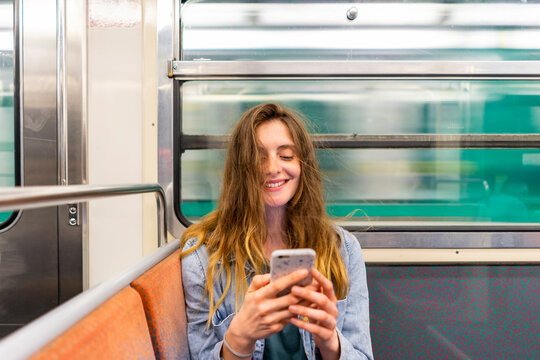 Portrait of smiling young woman in underground train looking at smartphone
