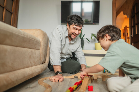 Father and son playing with toy train on living room floor