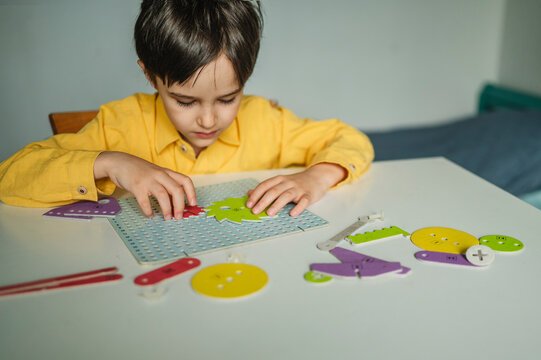 Focused boy learning by building a toy gear constructor at home