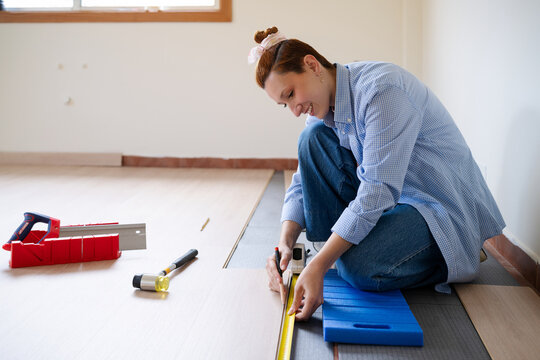 Youg woman measuring laminate flooring for a diy home renovation project