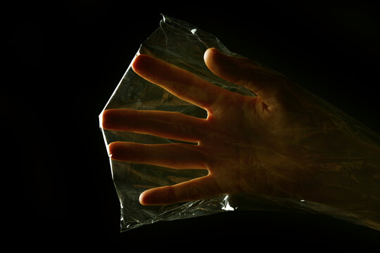Hand trapped inside a transparent plastic bag on black background