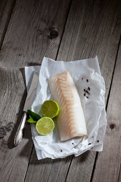 Filet of codfisch, lime and knife, and peppercorns on greaseproof paper on wood