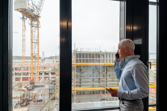 Architect calling on mobile phone in office overlooking construction