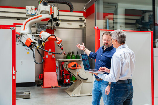 Employees planning with laptop near industrial robot in factory