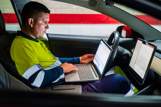 Male technician working on laptop for programming in electric car