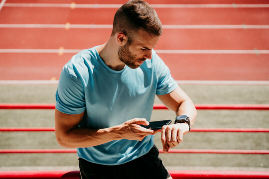 Male athlete in stadium checking smartwatch and smartphone