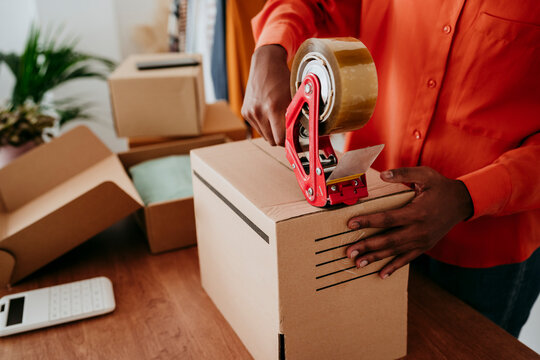 Hands of businesswoman sealing packages with tape at desk