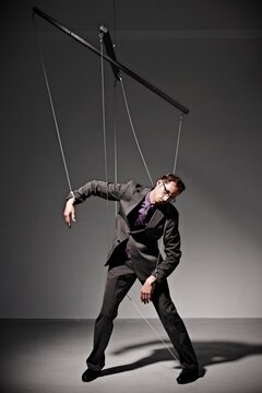 Businessman controlled like a puppet on strings in a studio