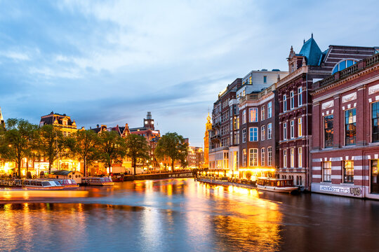 Illuminated buildings along a canal in Amsterdam at dusk
