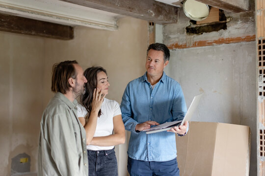 Mature couple with contractor discussing over laptop at construction site