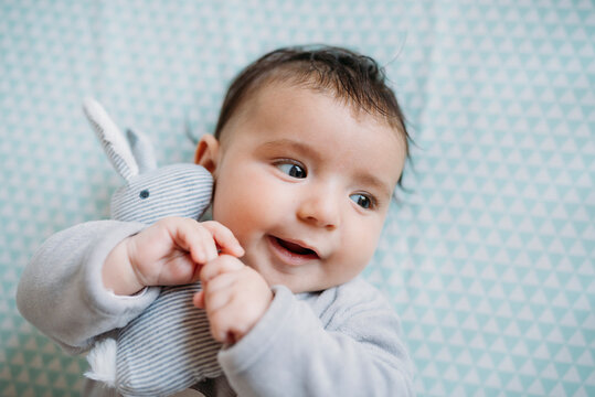 Portrait of smiling baby girl lying on bed cuddling with toy bunny