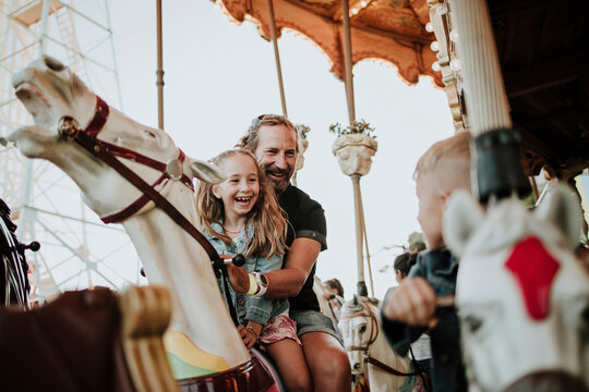 Happy girl enjoying carousel ride with father at amusement park