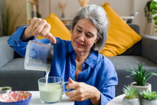Smiling woman pouring a green matcha latte at home
